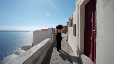 Santorini 'de siyah giyinmiş zarif bir kadın. Oia köyünün dar sokaklarında yürüyorum. Dünyanın en iyi günbatımı manzarasıyla tanınırım.