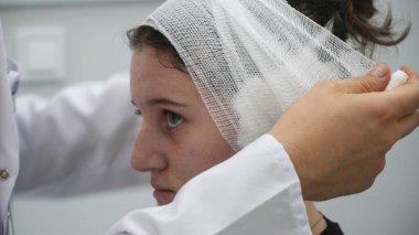 Doktor kulak ameliyatından sonra klinikteki baş hastaya bandaj yapıyor.