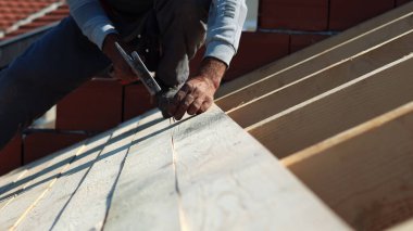 İnşaat işçisi marangoz çatıya çekiçle tahta çakıyor.