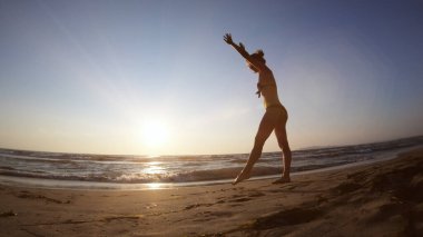 Gün batımında deniz kıyısında jimnastik yapan sağlıklı bir kadın.