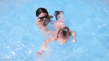 Mutlu aile annesi ve kızı gülümsüyor, yaz tatilinde havuzda yüzerken dönüyor.