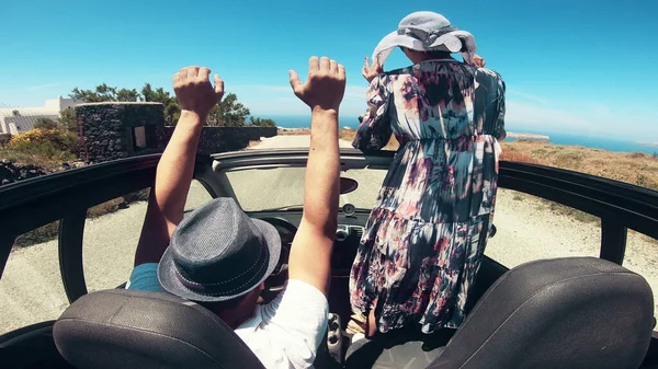 A young woman is driving by car to the sea and waving her hand from a convertible car. Vacation on the sea coast of Santorini island, greece