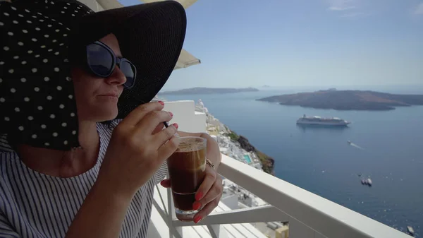 Woman Drinking Frappe Coffee on her vacation in Santorini, Greece. Amazng view of caldera and volcano from restaurant balcony