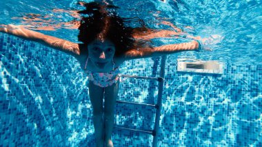 Mutlu küçük kız su altında komik suratlar yapıyor.