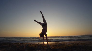 Gün batımında deniz kıyısında jimnastik yapan sağlıklı bir kadın.