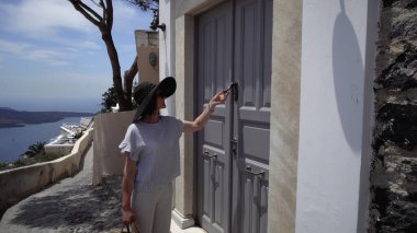 Kadın ziyaretçi Santorini caddesinde yürüyor ve eski kapı tokmağını çalıyor.