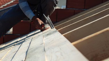 İnşaat işçisi marangoz çatıya çekiçle tahta çakıyor.