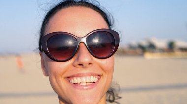 Kameraya gülümseyen ve onunla kumsalda dönen bir kızın portresi.