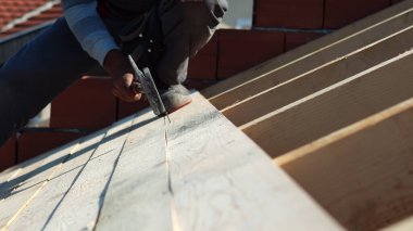 İnşaat işçisi marangoz çatıya çekiçle tahta çakıyor.