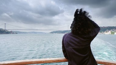 Genç kız gezgin İstanbul, Türkiye 'nin Avrupa ve Asya kesimlerini birbirine bağlayan köprüye doğru Boğaz üzerinde seyahat ederken dinleniyor.