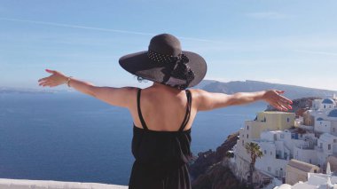 Zarif siyah elbiseli kadın el sallıyor ve Oia 'nın Santorini' deki romantik yaz tatilinin tadını çıkarıyor.