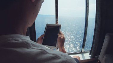 Lüks panoramik manzaralı feribot gezisi gemisinde dijital tablet bağlantısını izleyen turist. Denizde internet ve ev bağlantısı.