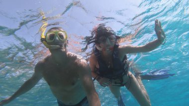 Mercan resif havuzunda balık okuluyla birlikte yüzen maske takan mutlu bir çift. Seyahat yaşam tarzı, su sporları açık hava macerası yaz tatillerinde yüzme dersleri.