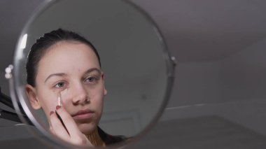 Yüzüne fondöten ya da allık süren bir kadın daire aynasına bakıyor.