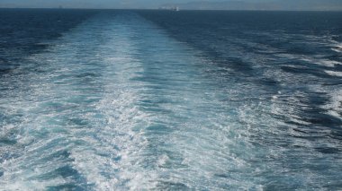 Halka açık bir feribotun arkasından gelen dalgalar suyun yüzeyinde köpük izi bırakır. Ufuk çizgisine kadar ilerler ve parlak suyu dalgalandırır.