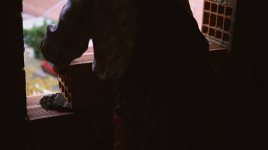 Duvar örmek için tuğla döşeyen bir duvarcı, malasıyla bir yerden harç çıkarıyor.