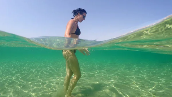 海のターコイズブルーの水の浅瀬で移動するファッションモデルの女の子のトレッキングショット — ストック写真