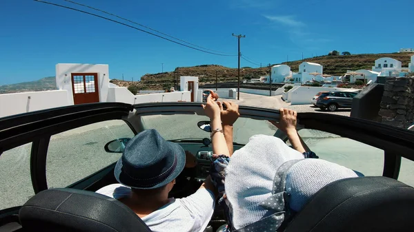 A young woman is driving by car to the sea and waving her hand from a convertible car. Vacation on the sea coast of Santorini island, greece