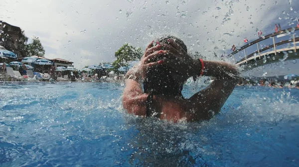 Portrait of beautiful woman relaxing on water jet drops falling down in swimming pool, slow motion