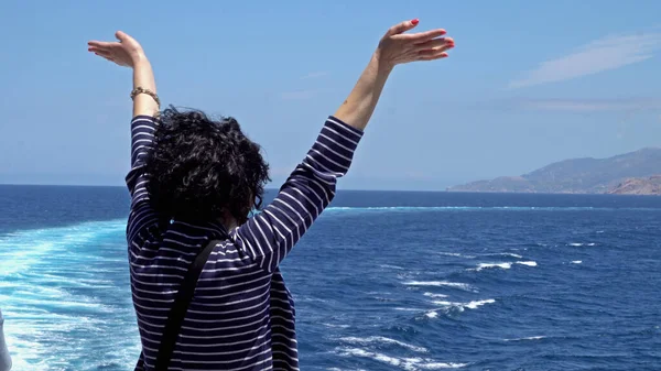 Cruise ship passenger in Santorini waving hands saying hello while sailing on ferry. Santorini is a famous Alaska cruise ship destination for travel sightseeing.