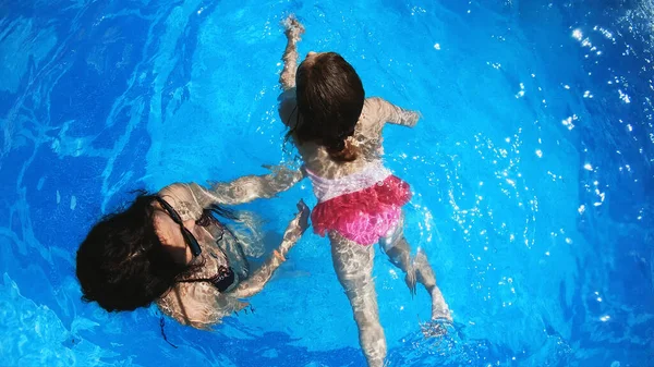 Beautiful woman give swimming lessons to her daughter in swimming pool