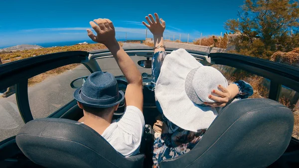 A young woman is driving by car to the sea and waving her hand from a convertible car. Vacation on the sea coast of Santorini island, greece