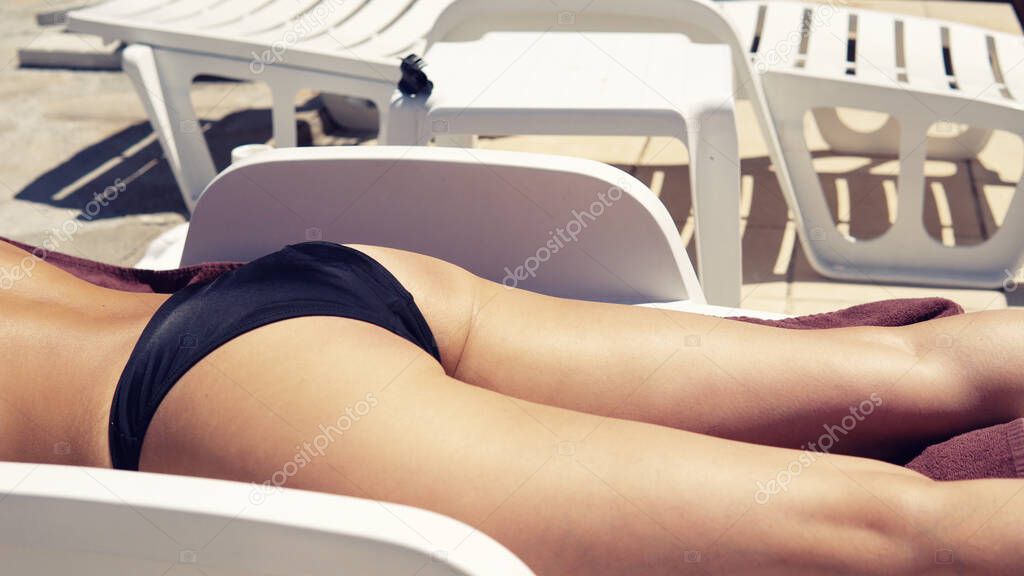Sexy beautiful girl with curly hair sunbathing by the pool