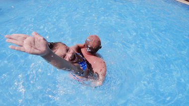 Baba ve kızı yüzme havuzunda kızın biriyle oynuyorlar.