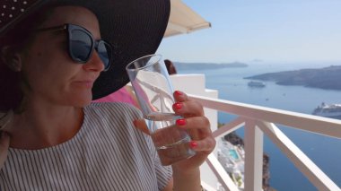 Lüks otel terasında su ve kahve içen Santorini manzaralı kadın.