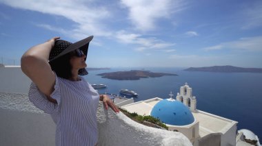 Fira, Santorini, Yunanistan 'daki Fira kilisesinin üç çanı yakınında gülümseyen mutlu esmer kadın.