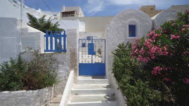 Beyaz Saray 'ın avlusunda mavi metal kapılar ve bahar çiçekleri olan bir giriş. Yunanistan 'ın Santorini adasında çekildi