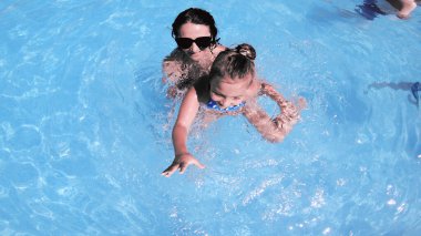 Mutlu aile annesi ve kızı gülümsüyor, yaz tatilinde havuzda yüzerken dönüyor.