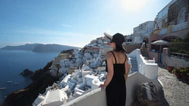 Şık ve şık giyinen siyah elbiseli mutlu kadın Santorini, Yunanistan 'da tatilinin tadını çıkarıyor.