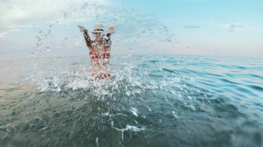 Hasır şapkalı güzel bir kızın yavaşça denize dalması ve kameraya doğru sıçraması. 