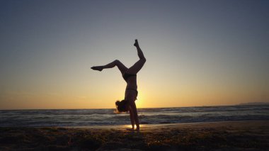 Gün batımında deniz kıyısında jimnastik yapan sağlıklı bir kadın.