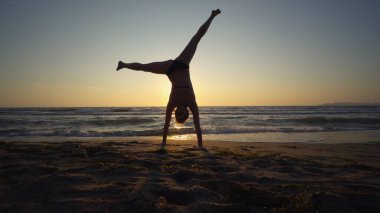 Gün batımında deniz kıyısında jimnastik yapan sağlıklı bir kadın.