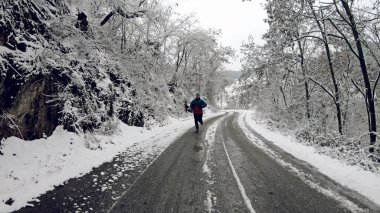 Genç sağlıklı sporcu karlı dağ yolunda asfalt yolda koşuyor.