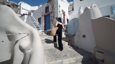 Santorini 'de siyah merdivenleri çıkan zarif bir kadın. Genç bir bayan yaz tatilinde Santorini 'de. O, Oia 'daki ünlü turistik eğlenceyi ziyaret ediyor.