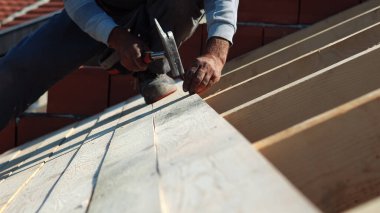 İnşaat işçisi marangoz çatıya çekiçle tahta çakıyor.