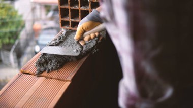 Duvar örmek için tuğla döşeyen bir duvarcı, malasıyla bir yerden harç çıkarıyor.