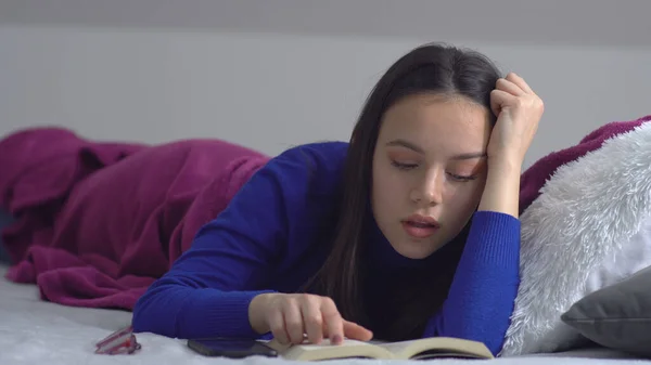 年轻女人躺在床上看书 — 图库照片