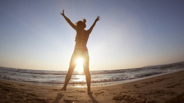 Healthy woman on seashore at sunset doing gymnastics exercises