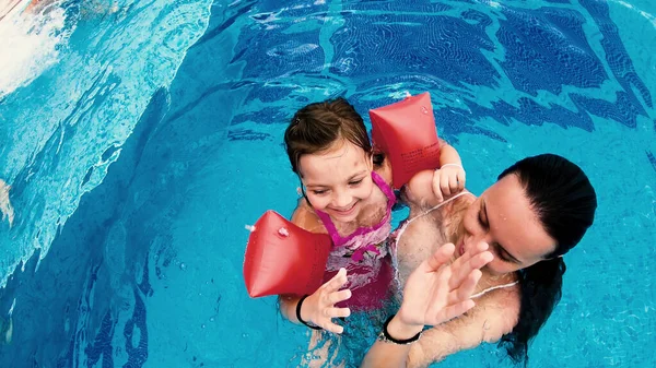 Teen whisper funny story to her little sister with inflatable arm bands relaxing in pool and giving high five