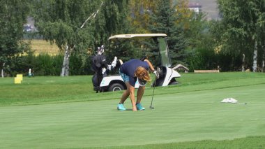 Bansko, Bulgaristan - 20 Ağustos 2019: Kadın golfçü atışı kaçırmadan önce çömeldi ve yeşili inceledi