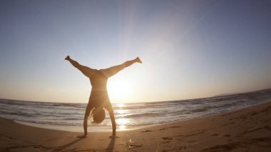 Gün batımında deniz kıyısında jimnastik yapan sağlıklı bir kadın.