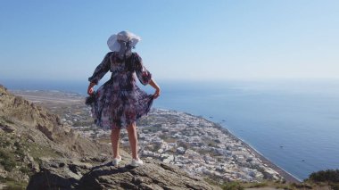 Mutlu kadın turist Santorini 'de neşe içinde kıvranırken eğleniyor. Antik Thera dağ arkeoloji alanındaki Kamari 'nin panoramik görüntüsü, yavaş çekim