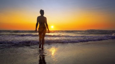 Siluet güçlü kendine güveni olan kadın gün doğumunda deniz kenarında kollarını açar.