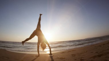 Gün batımında deniz kıyısında jimnastik yapan sağlıklı bir kadın.