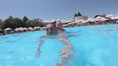 Baba ve kızı yüzme havuzunda kızın biriyle oynuyorlar.