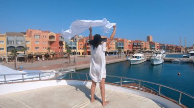 Lüks yat güvertesinde duran beyaz elbiseli manken kadın. Hurghada, Mısır 'daki iskelenin panoramik manzarası